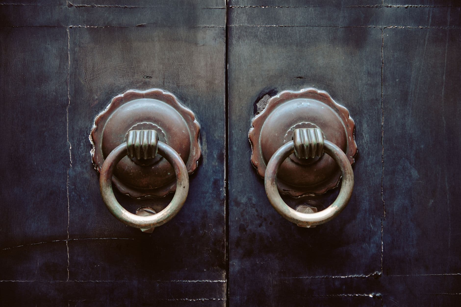 Dos aldabas de metal sobre una puerta oscura.